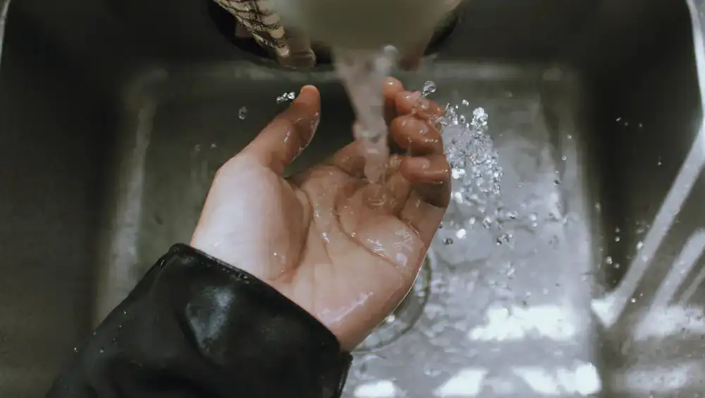 Hands washing a chef knife blade under a gentle stream of warm water in a clean kitchen sink