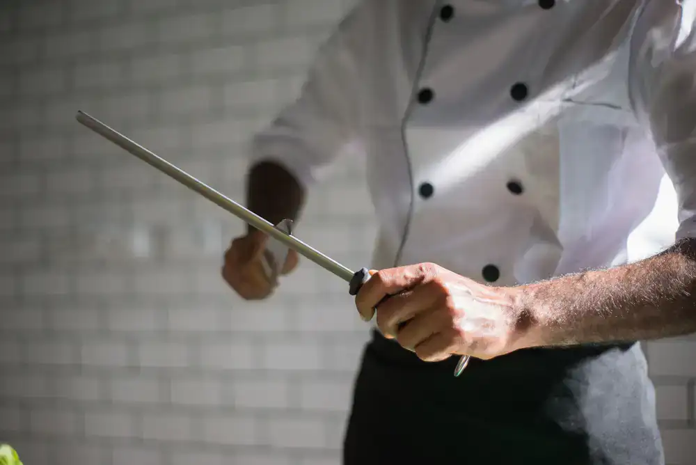 A person carefully swiping a steel knife against a ceramic honing rod to align the edge