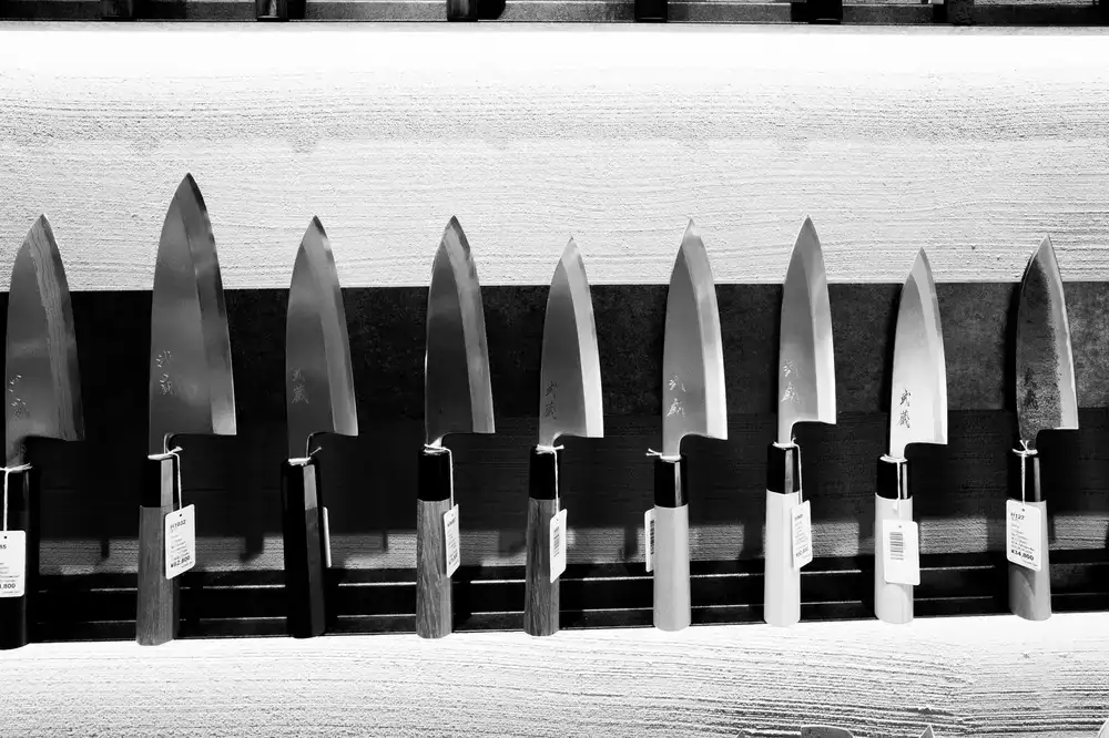 Three high-end chef knives securely attached to a sleek wooden magnetic knife strip mounted on a kitchen wall